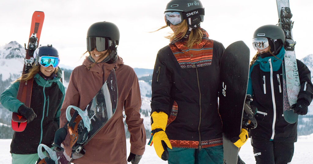 Group of four women walking with skis and snowboards.