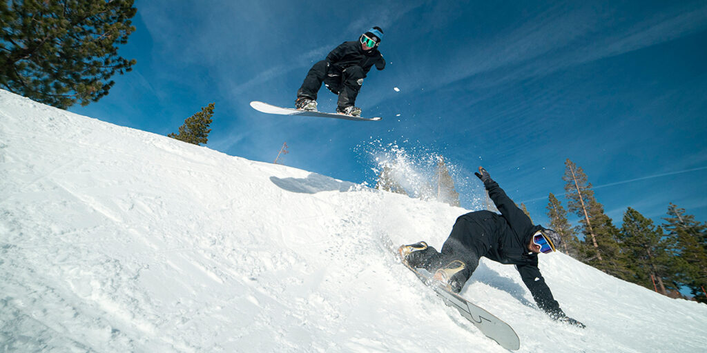 Two snowboarders make a slash turn