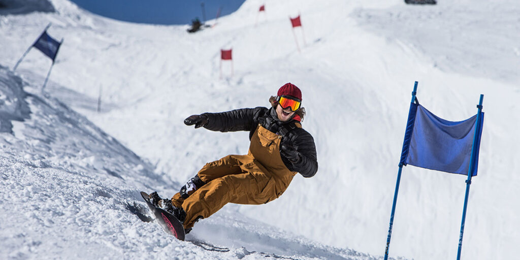 Snowboarder smiling while he turns around a banked slalom gate