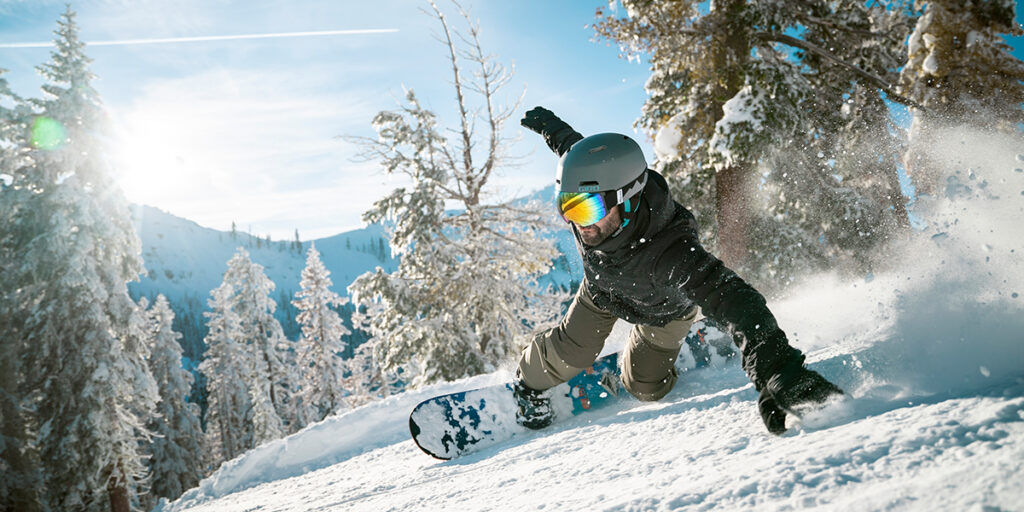 Snowboarder slashes a turn with snowy trees in the background