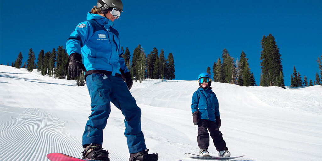 a young boy snowboarding with his instructor