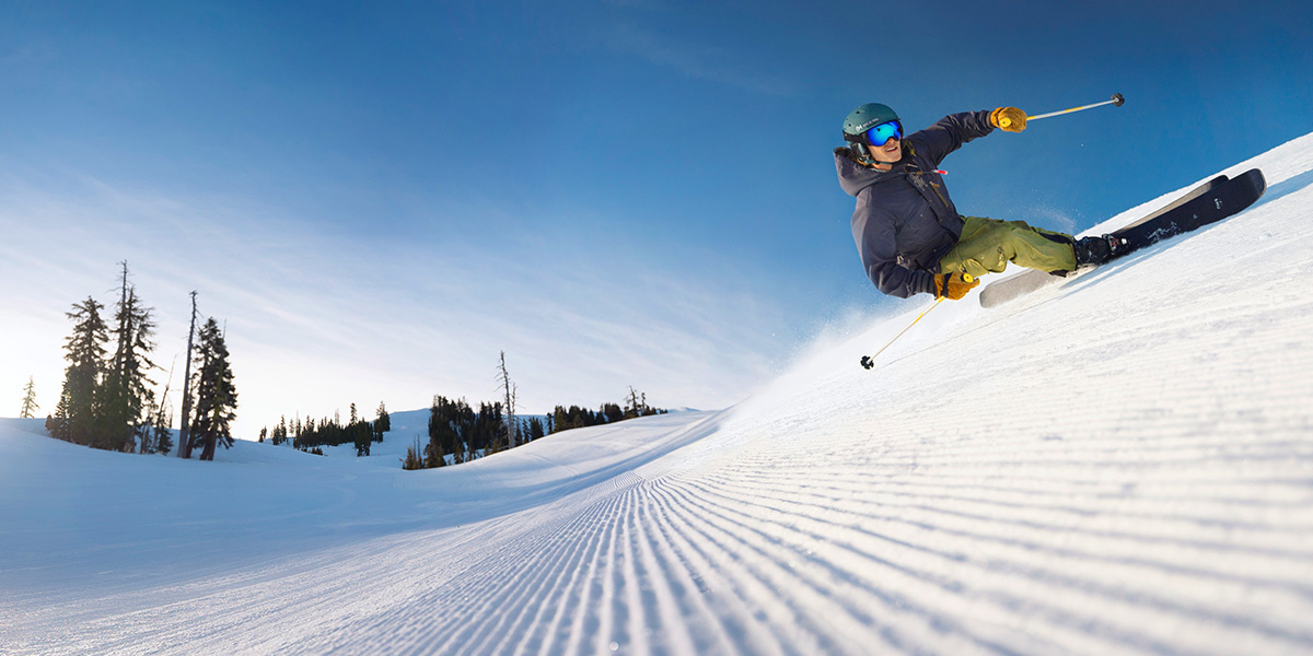 A skier carves a turn on a fresh corduroy slope.