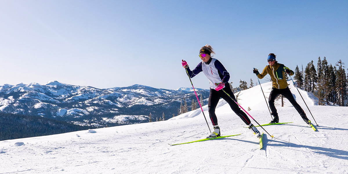 Two skate ski cross country skiers on trail at Royal Gorge with a beautiful view of the Sierra Crest.